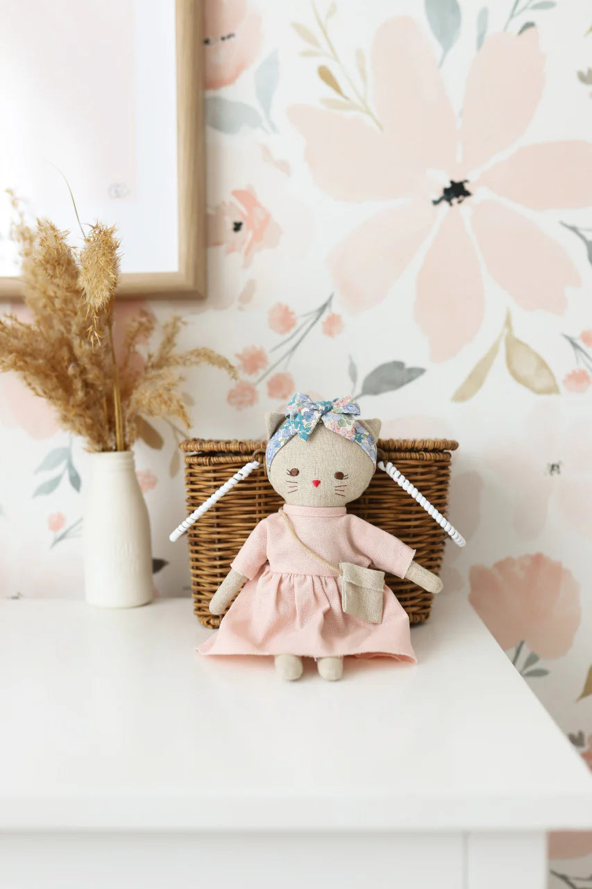Stuffed toy in a pink dress on a white surface with floral wallpaper in the background