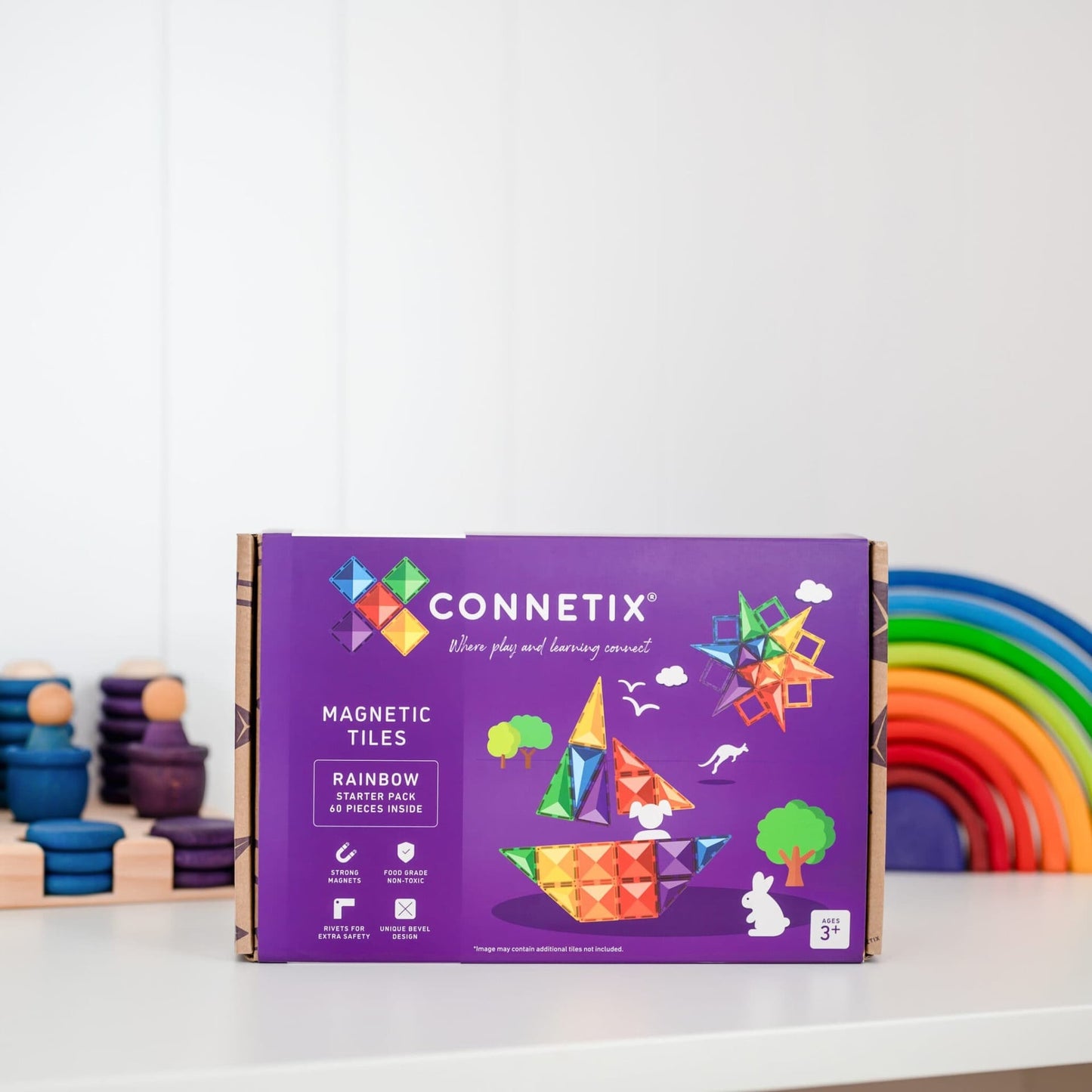 Purple Connetix magnetic tiles packaging on a white surface with colorful toys in the background.