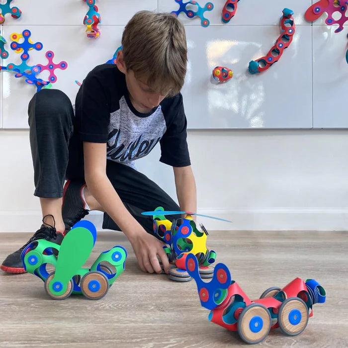 Child playing with colorful toy cars on a wooden floor.