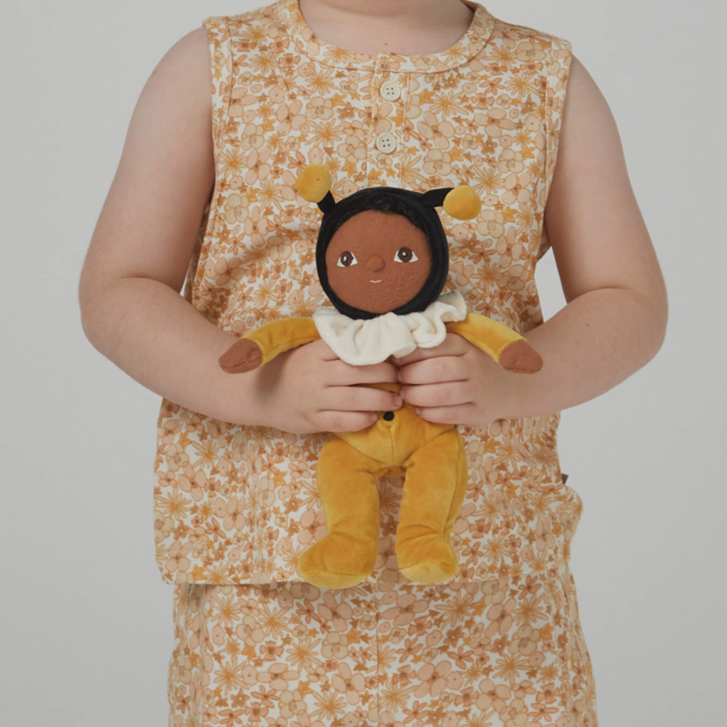 Child wearing a floral dress holding a plush toy with a neutral background