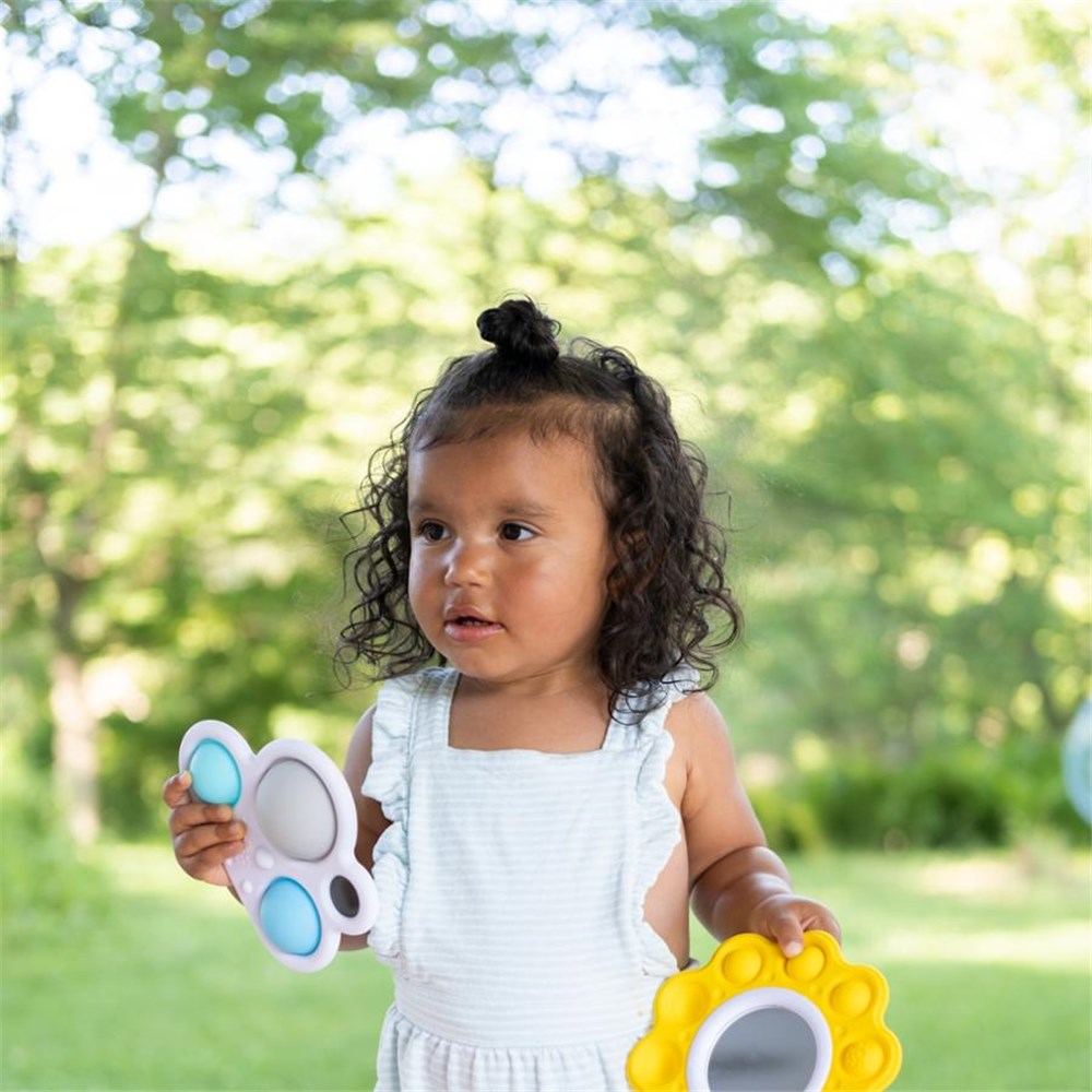 Child holding a colorful toy outdoors with greenery in the background