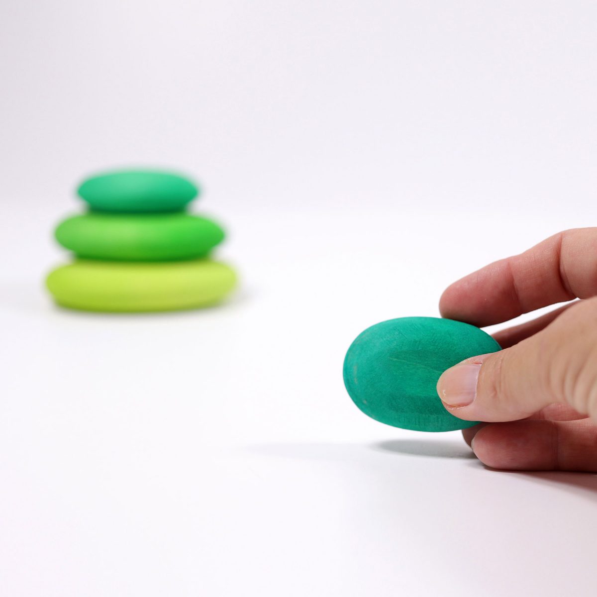Hand holding a green stone with a stack of stones in the background on a white surface