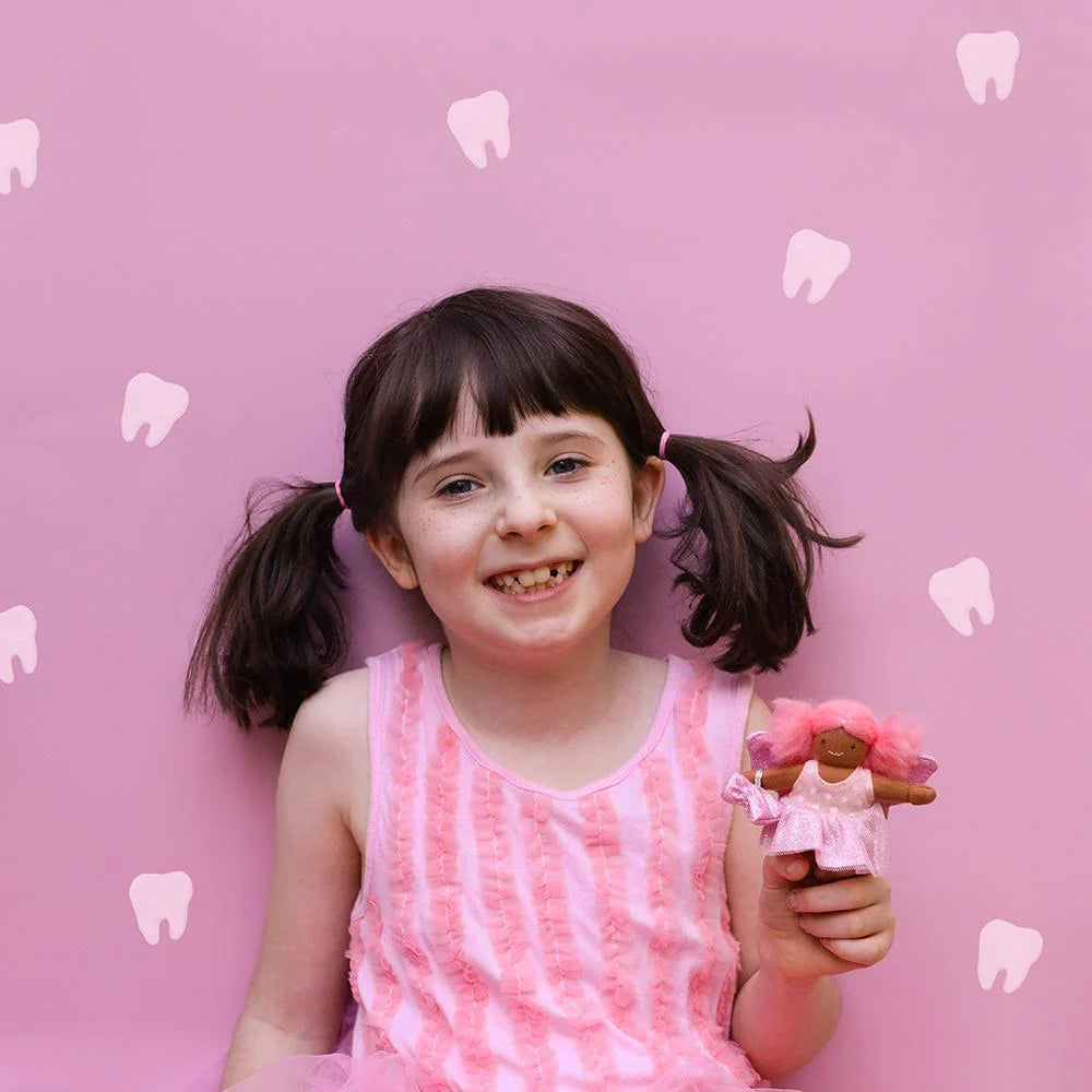 Young girl with pigtails holding a doll against a pink background with tooth illustrations
