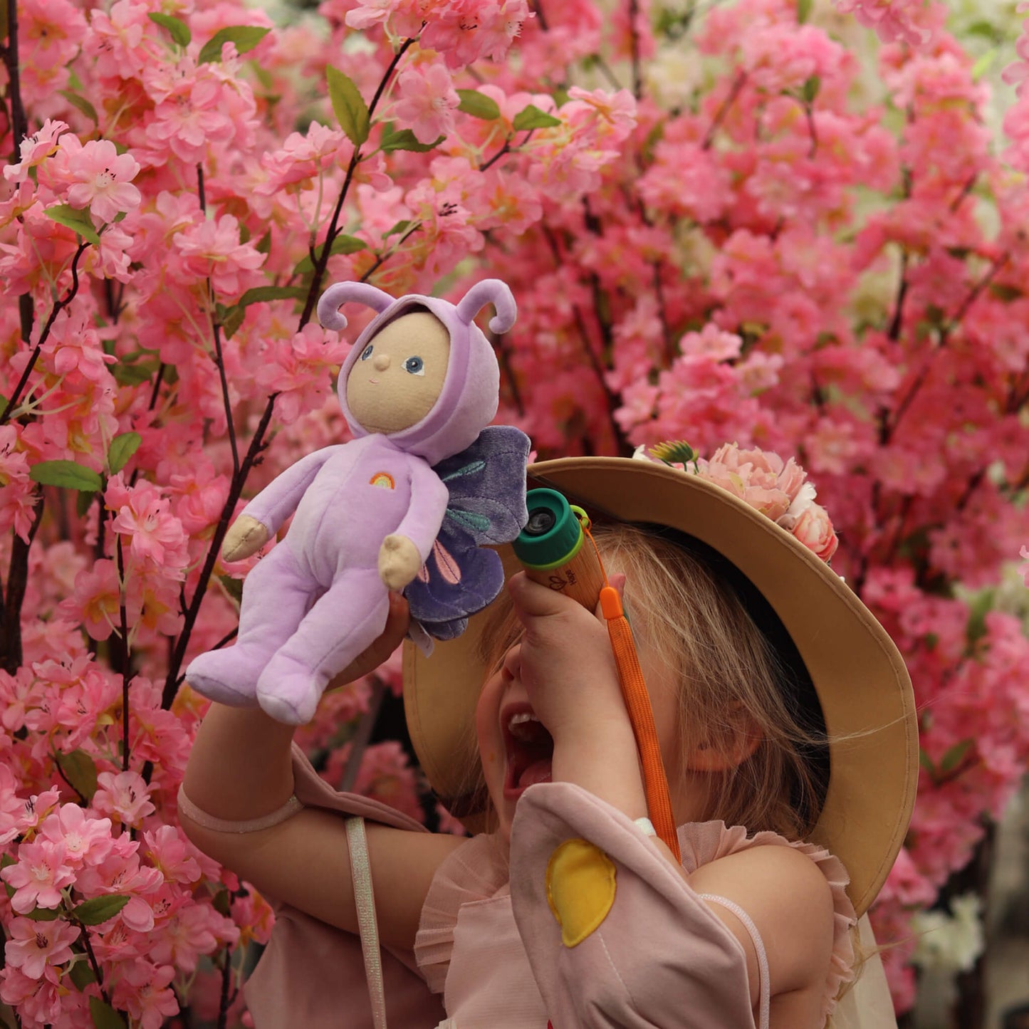 Child holding a plush toy in front of pink cherry blossoms