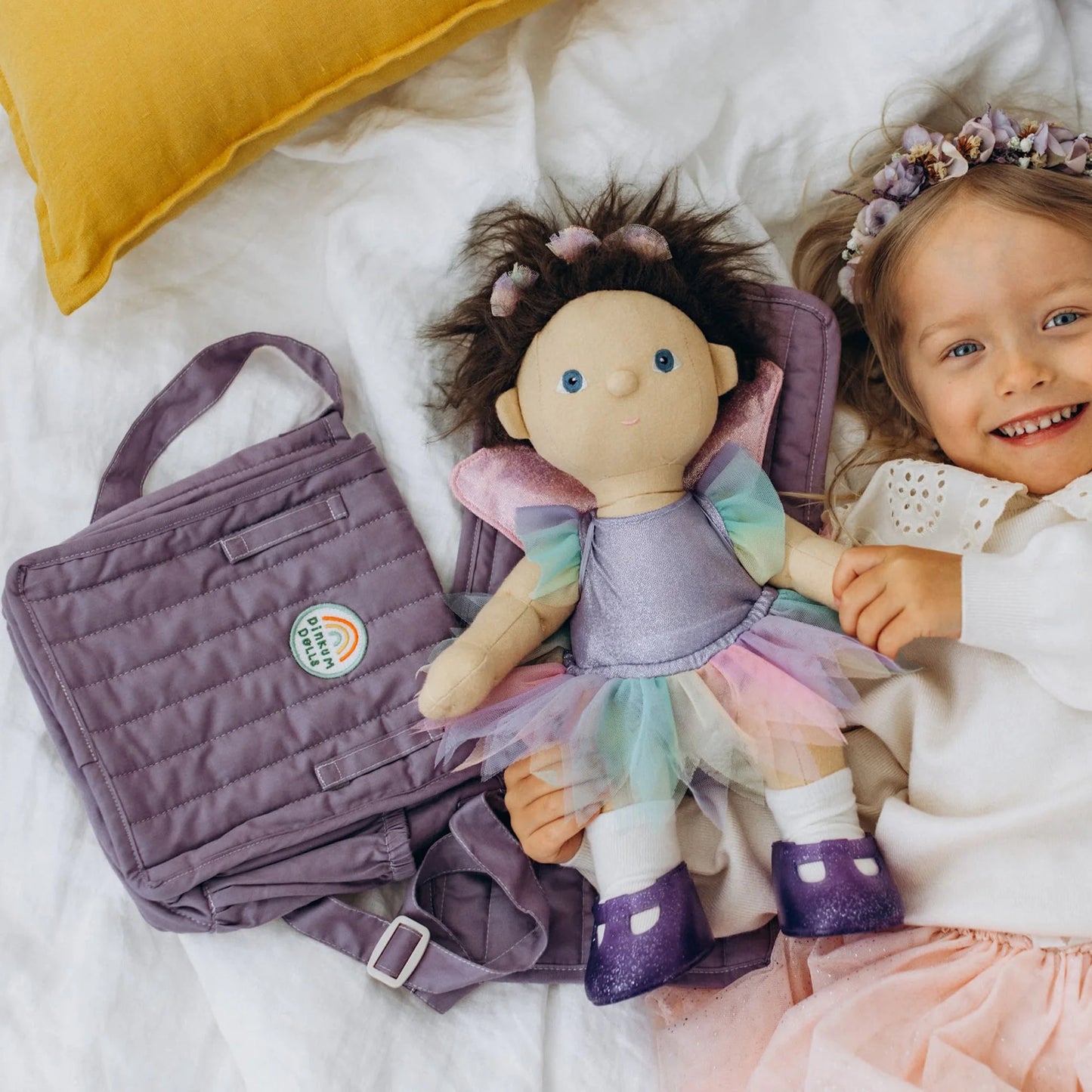 Child with a doll and a purple bag on a white blanket