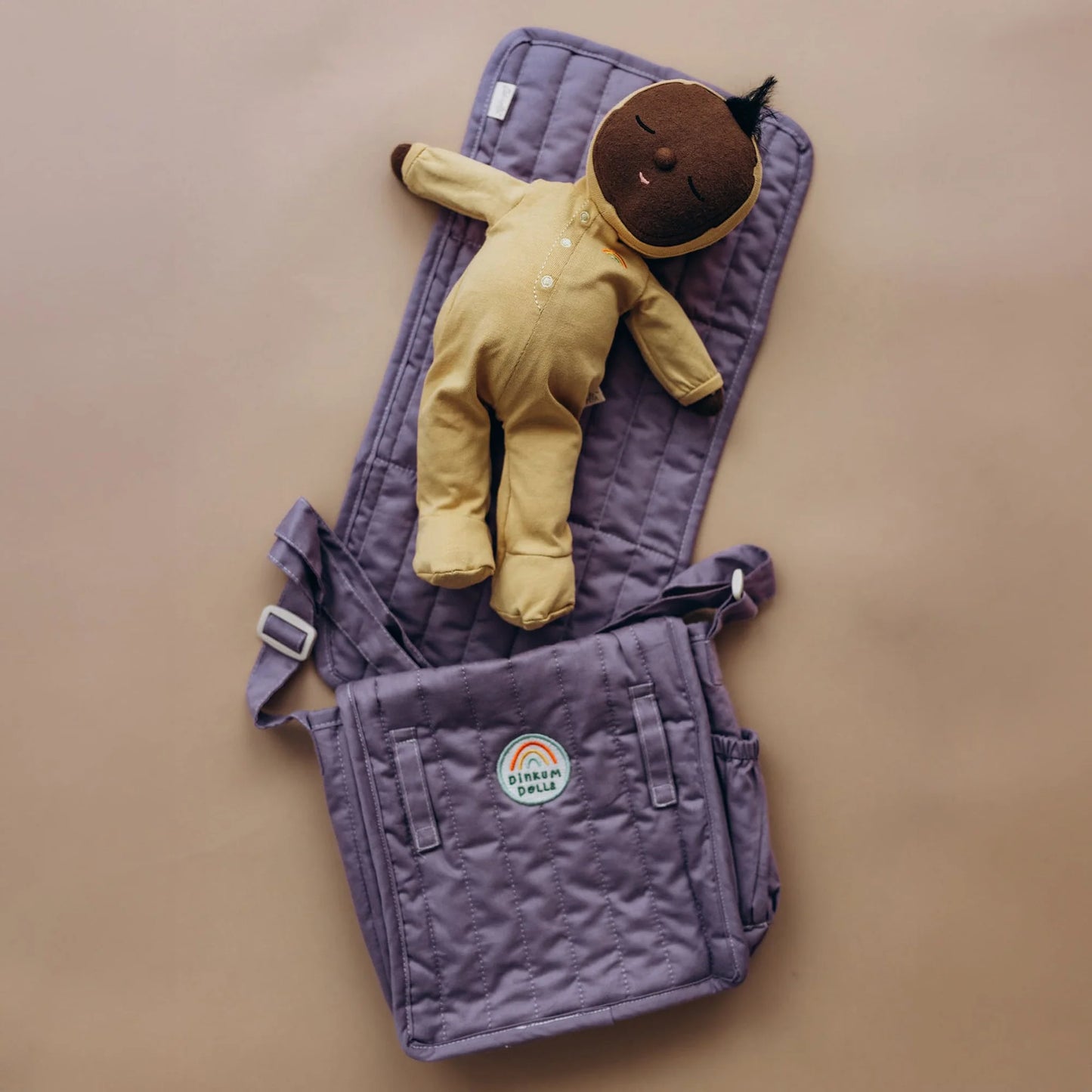 Purple baby carrier with a yellow baby outfit on a beige background