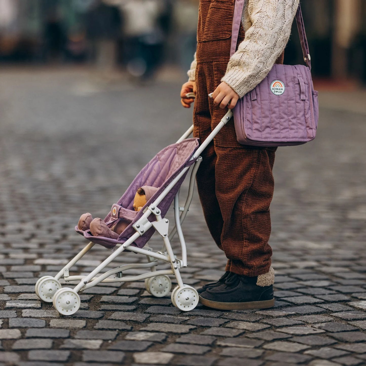 Person pushing a purple stroller with matching bag on a cobblestone street
