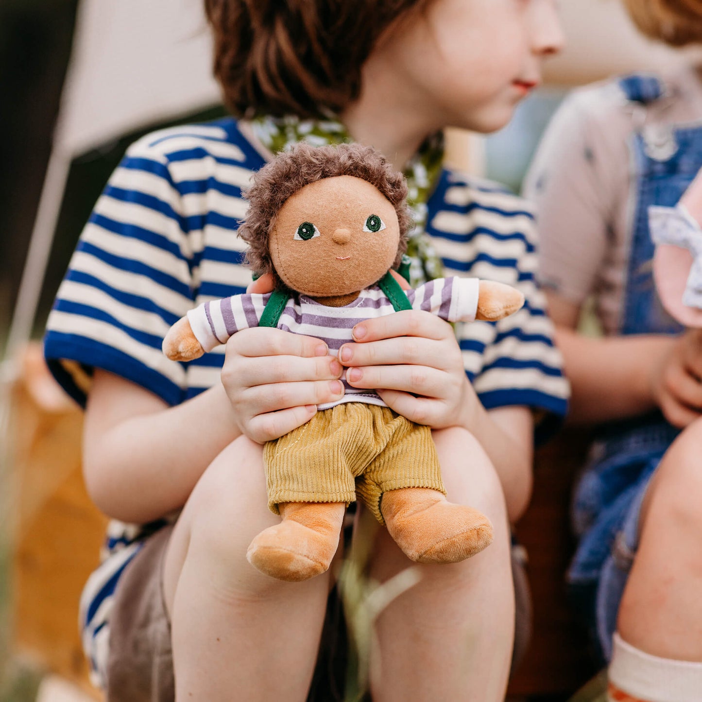 Person holding a small doll with another person in the background