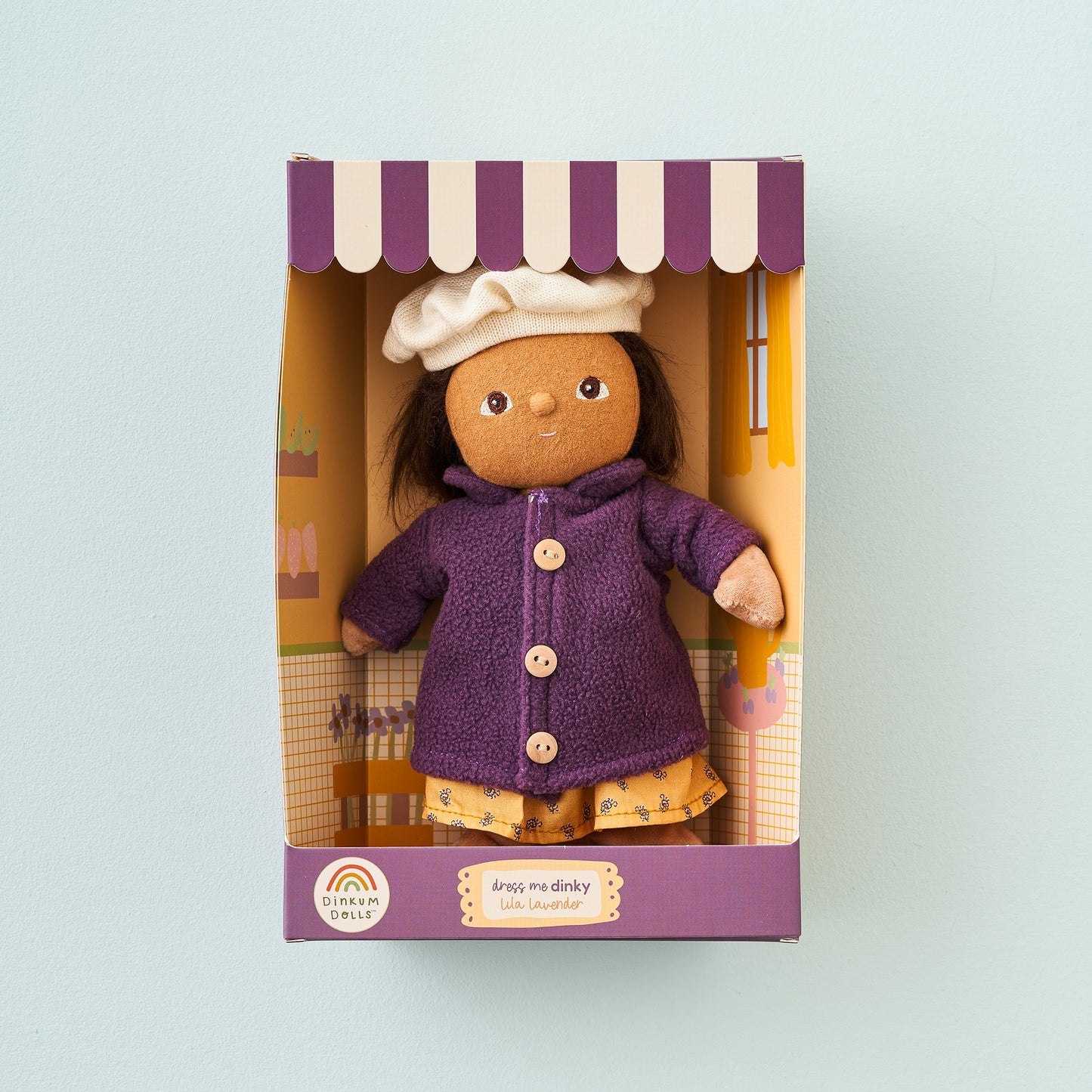 Toy doll in a purple outfit with a white hat in a box on a light blue background
