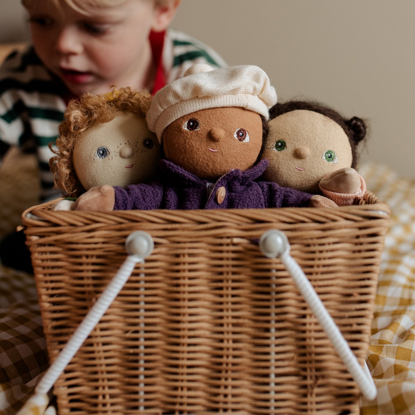 Three dolls with different hair colors and outfits inside a wicker basket, with a child partially visible.