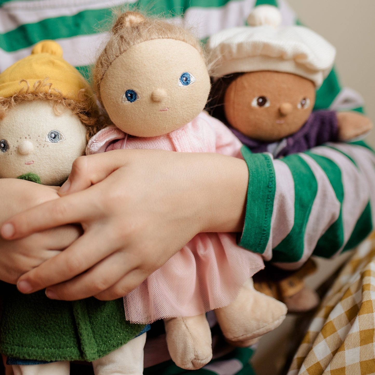 Child holding three small dolls with different outfits and hairstyles.
