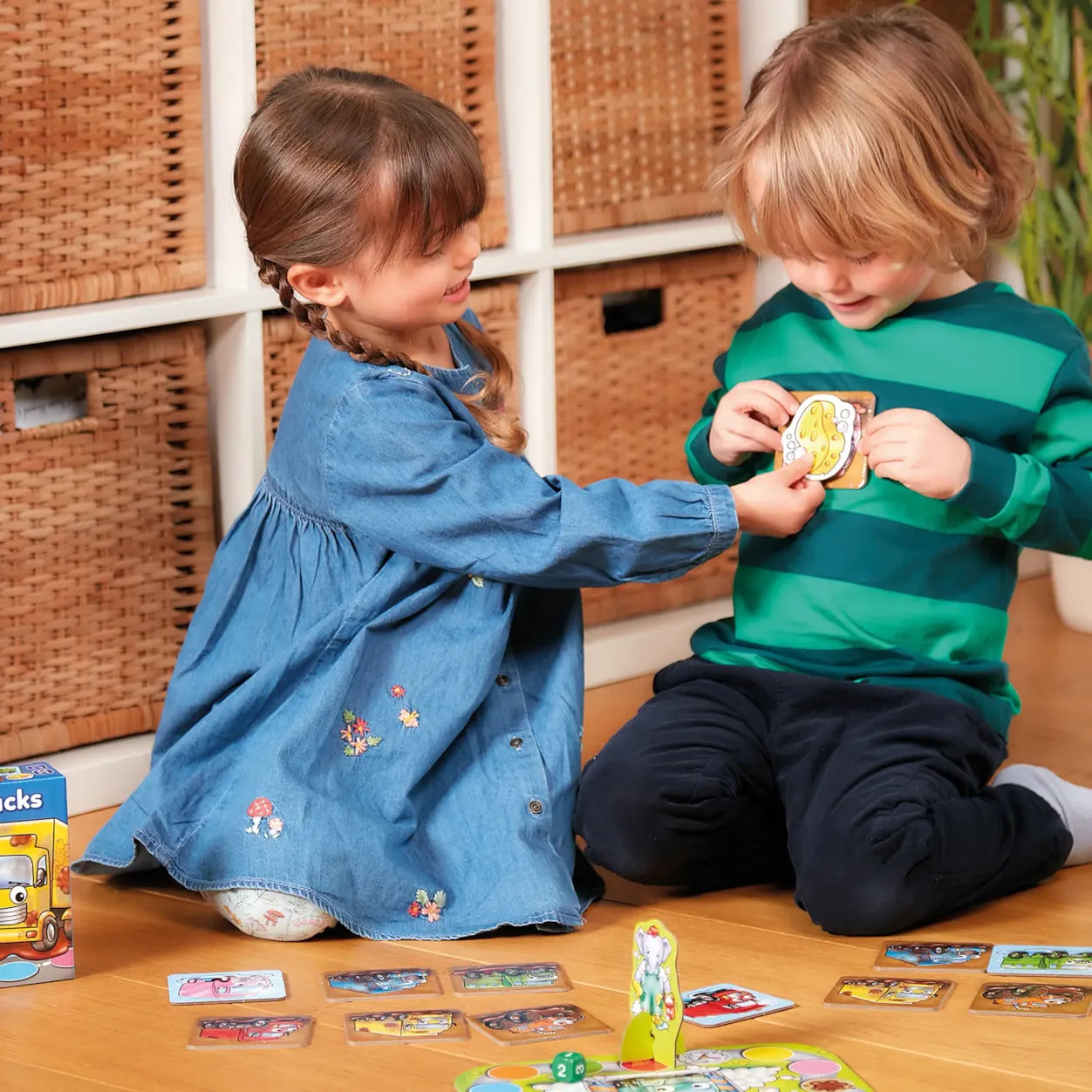 Two children playing with cards on the floor in a room with wicker baskets.