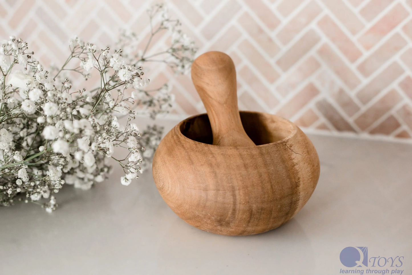 Wooden mortar and pestle on a neutral background with baby's breath flowers.