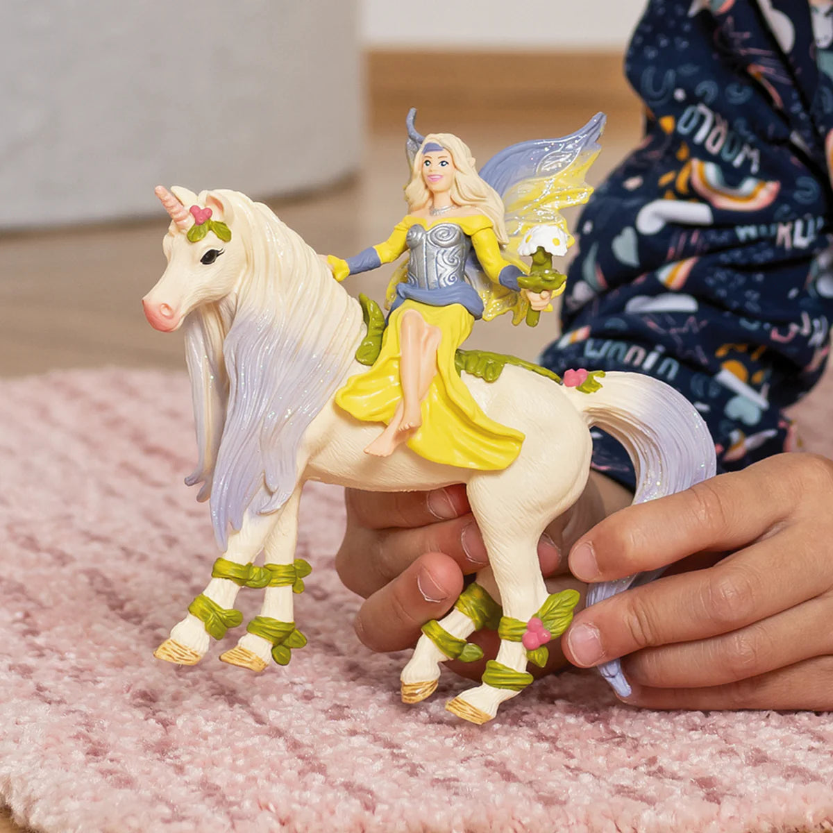 Toy fairy and unicorn figure held by a child on a pink surface