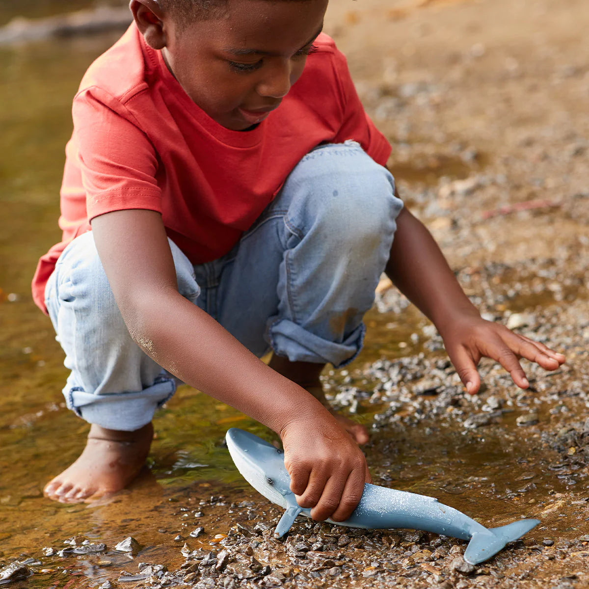Child playing with a toy whale by a body of water