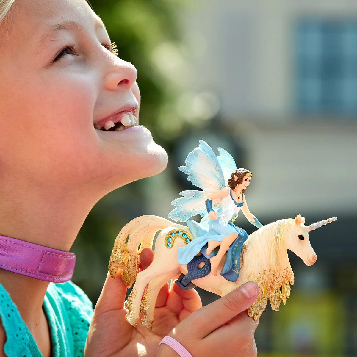 Child holding a toy fairy on a unicorn with a blurred outdoor background