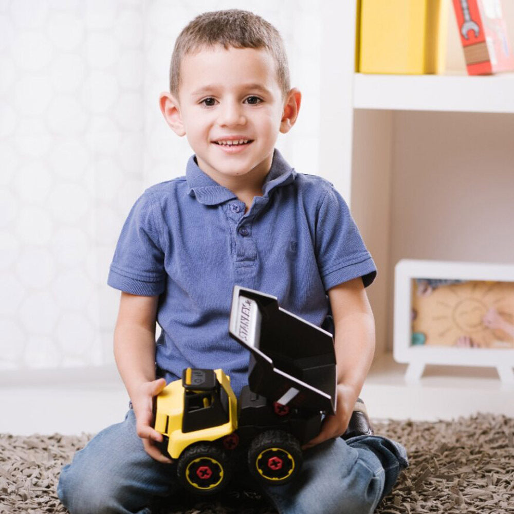 Child holding toy dump truck in a room with a shelf in the background