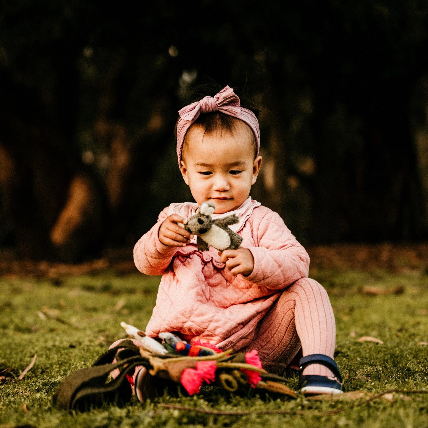 Child in pink outfit holding a finger puppet in a natural setting