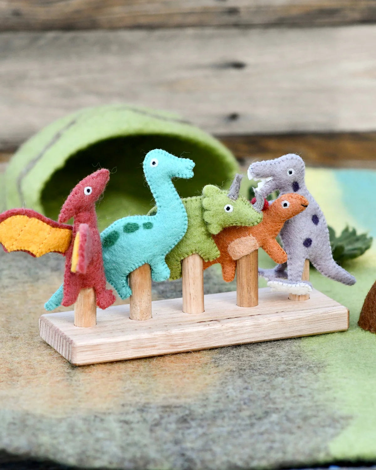 Set of colorful felt dinosaurs on a wooden stand with a wooden background