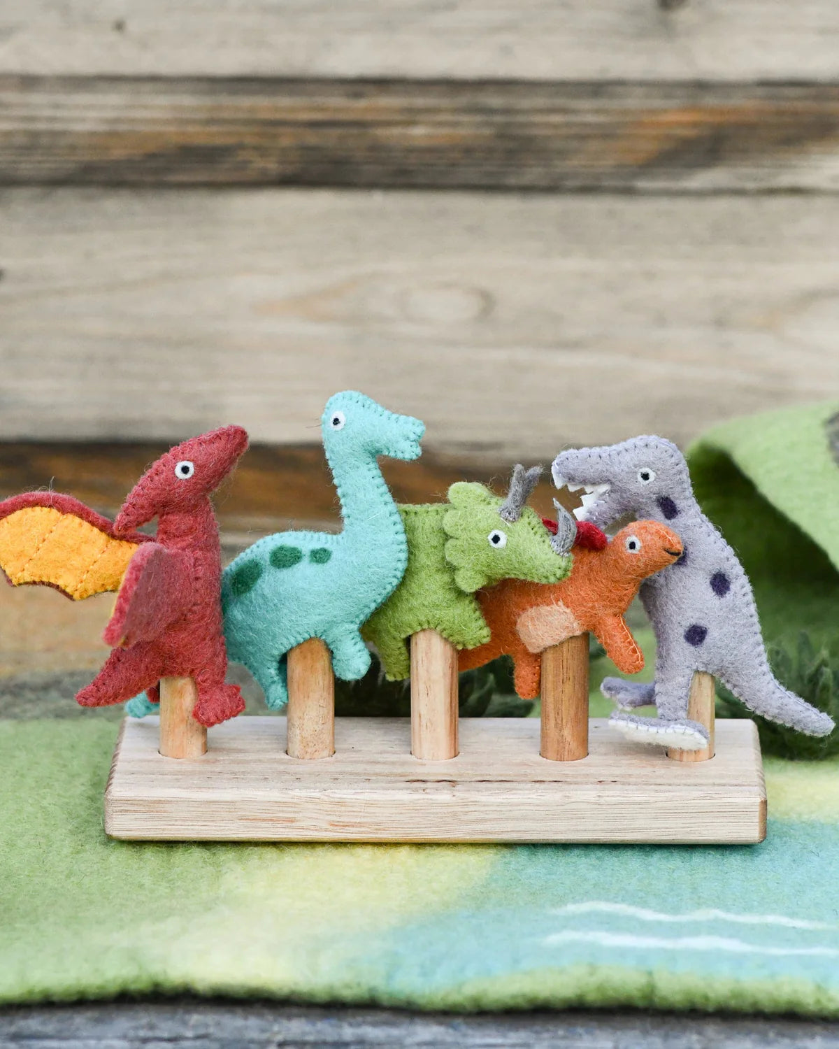 Set of colorful felt dinosaurs on a wooden stand with a natural wood background