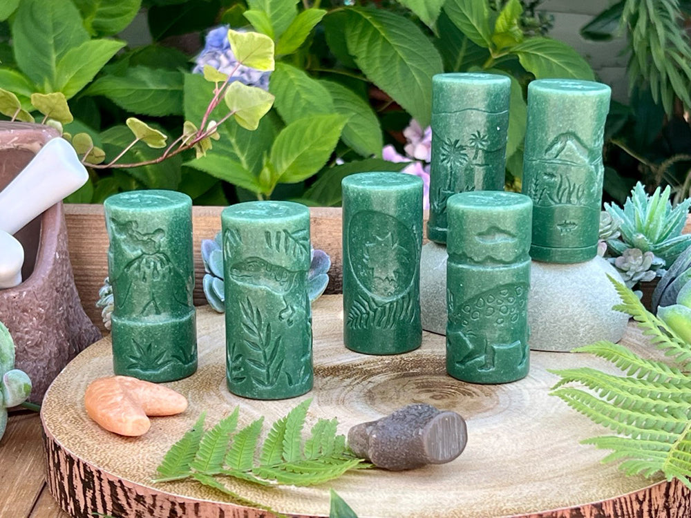 Set of green rollers with embossed designs on a wooden surface with plants in the background
