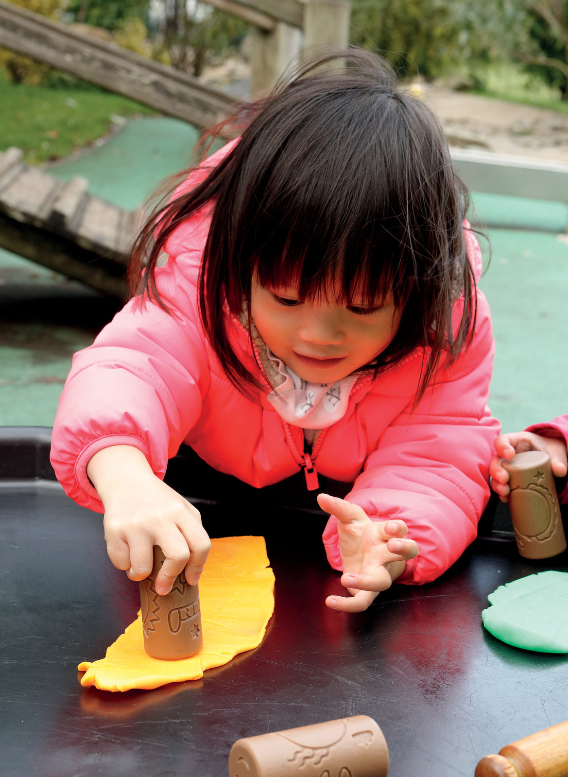 Child playing with play dough and rollers on black surface