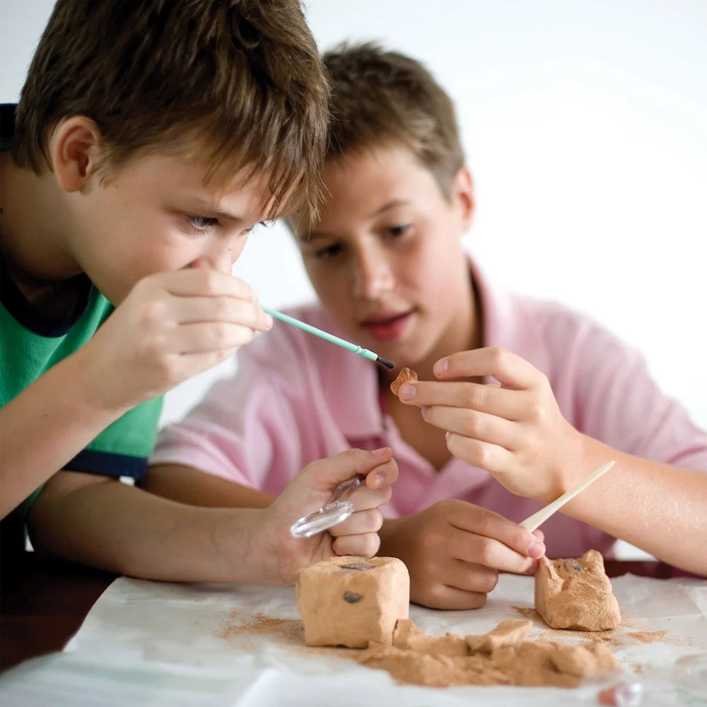 Two children engaged in a craft activity with sand and tools on a table.