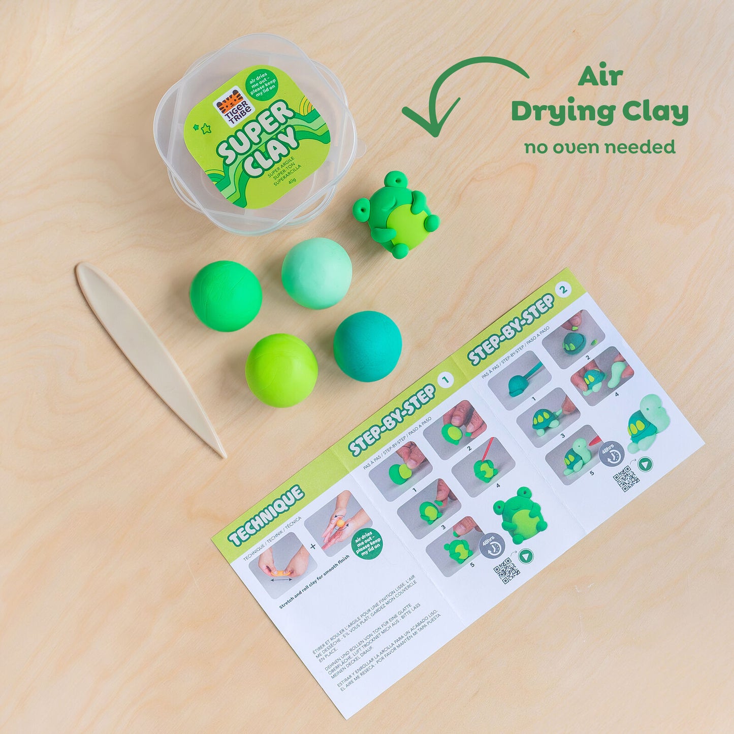 Super Clay packaging with green and blue clay balls and a step-by-step guide on a wooden surface.