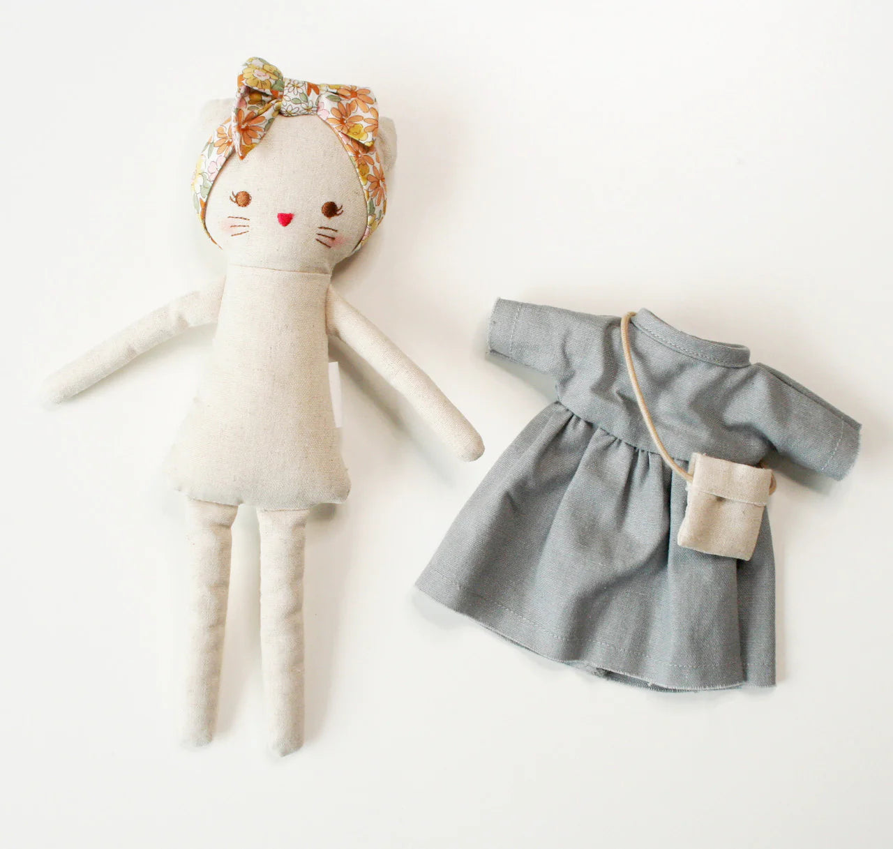 White doll cat with a colourful bow and a gray dress on a white background
