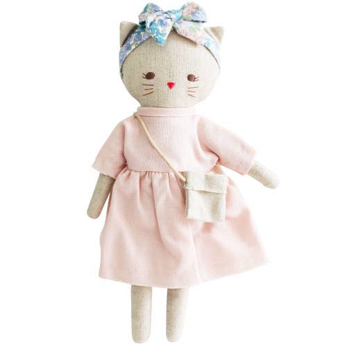 A small doll resembling a kitten with a pink linen dress and a floral headband, also carrying a small bag.