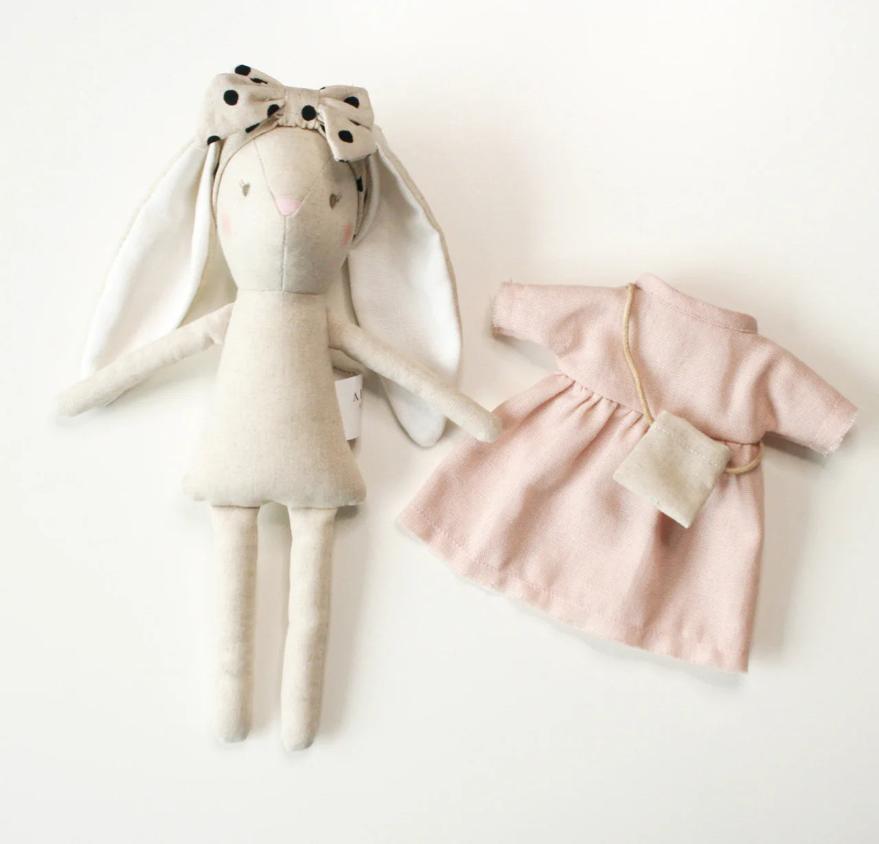 Stuffed bunny toy with a polka dot bow and a pink dress on a white background