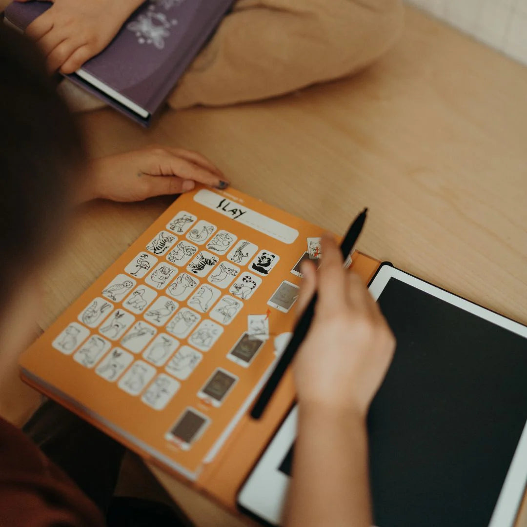 Person using a communication board with symbols and a pen on a wooden table.