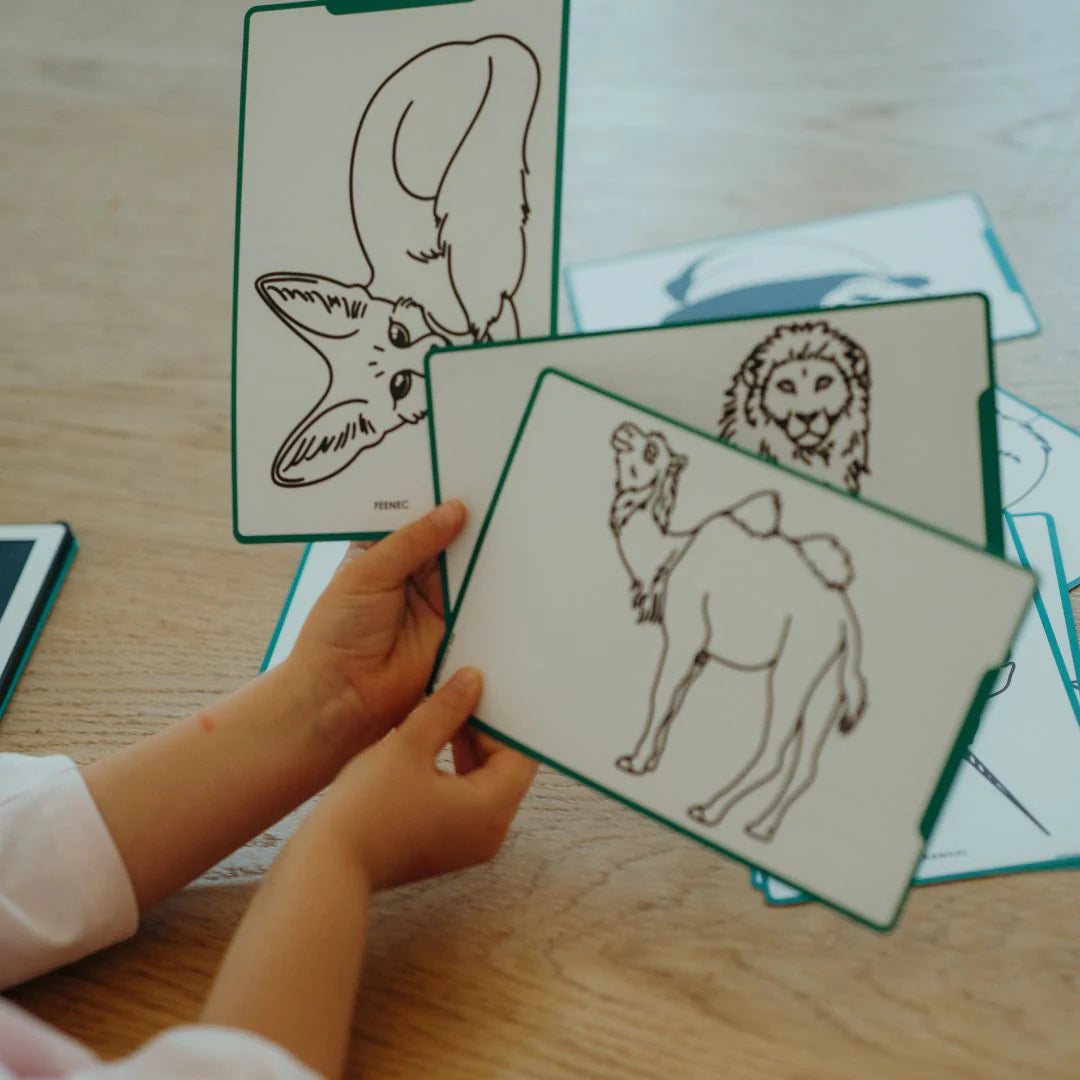 Child holding a card with a lion illustration among other animal cards on a wooden surface.