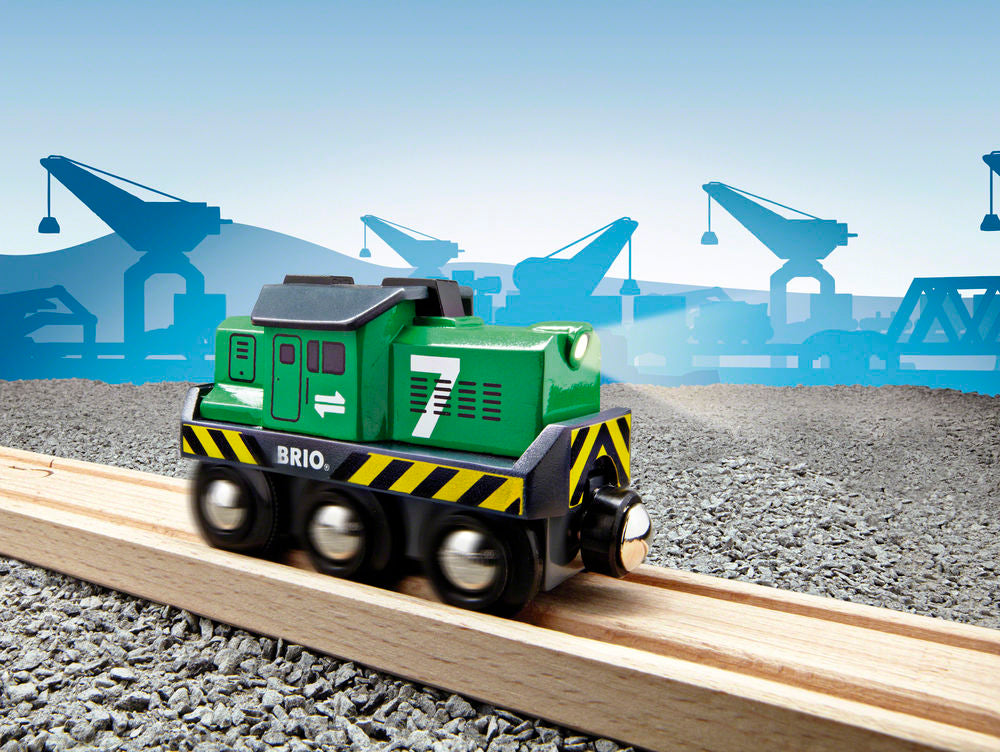 Green toy train on a track with cranes in the background