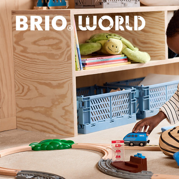 Child playing with a toy train set on a wooden floor, with 'Brio World' branding.