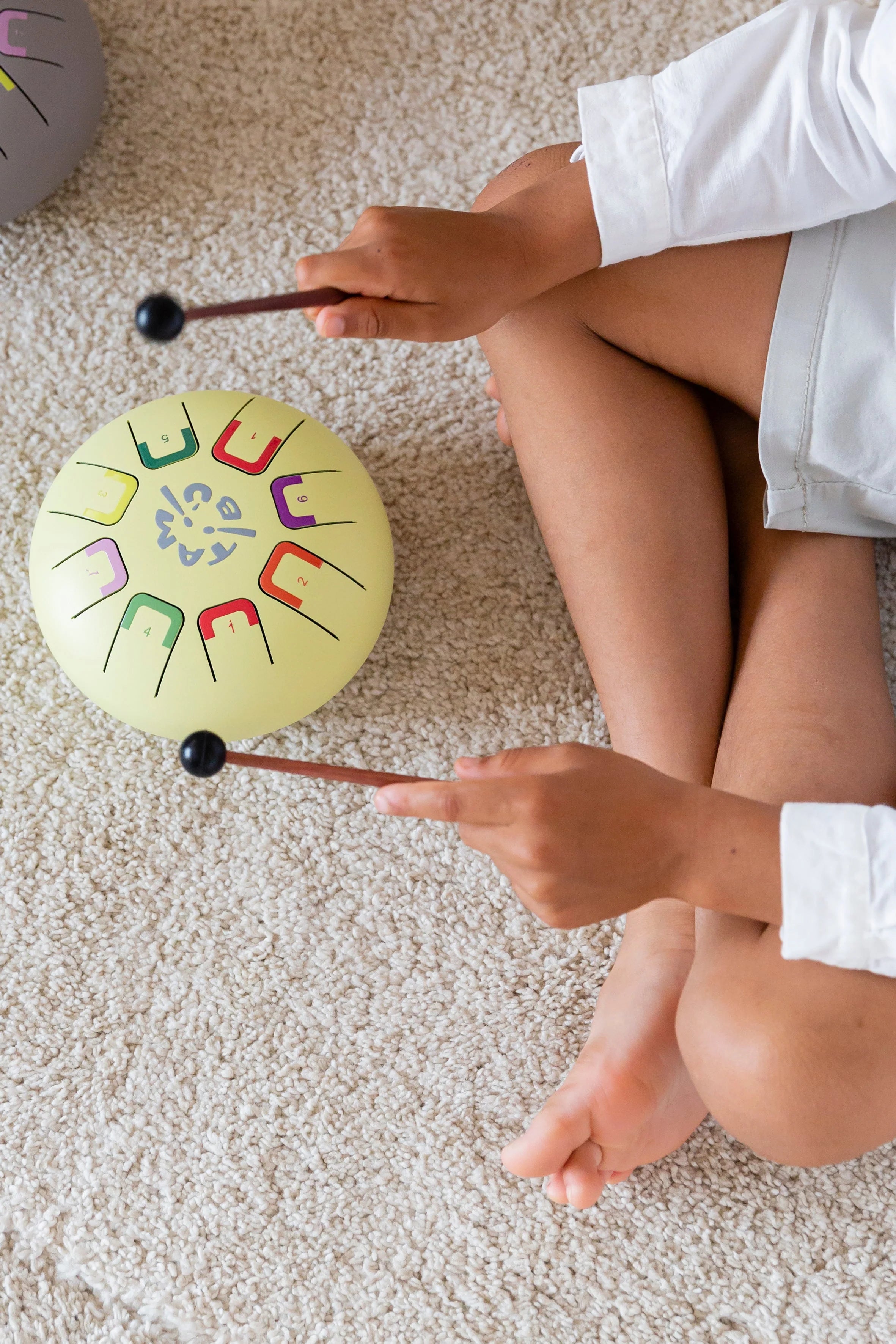 Person playing a colorful handpan drum on a carpeted floor
