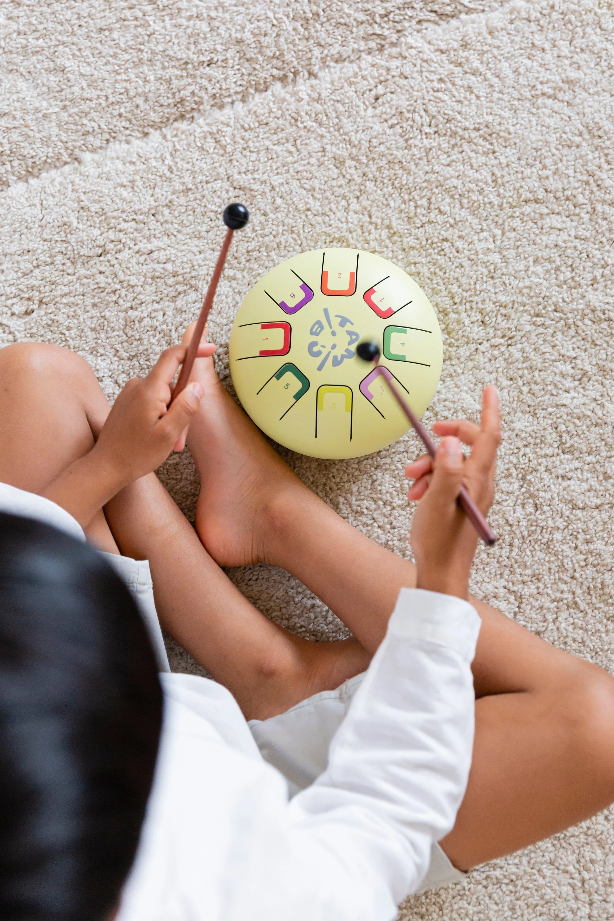 Person playing a colorful handpan drum on a carpeted floor