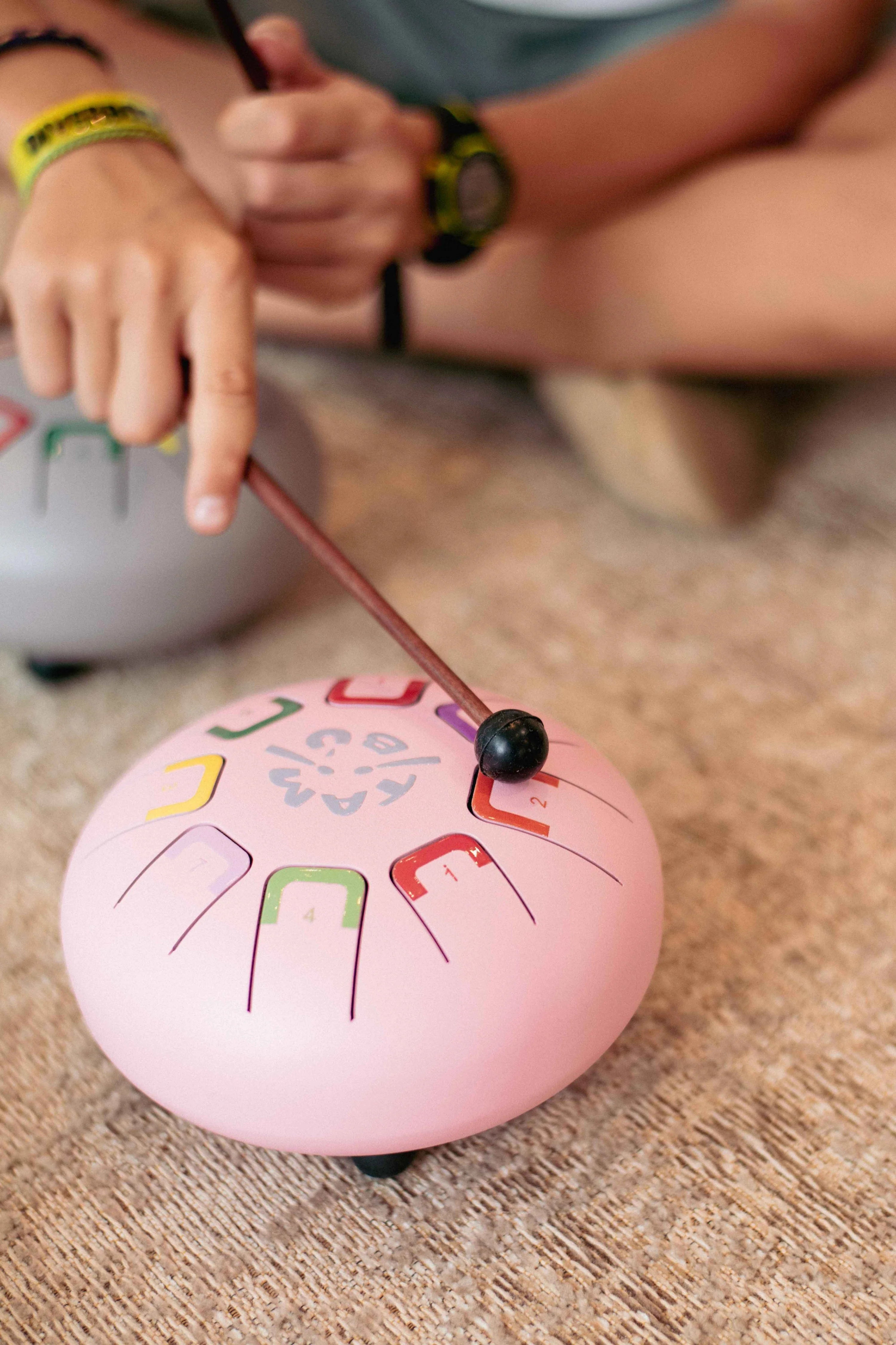 Pink hand drum with colorful designs on a wooden surface, being played by a child.