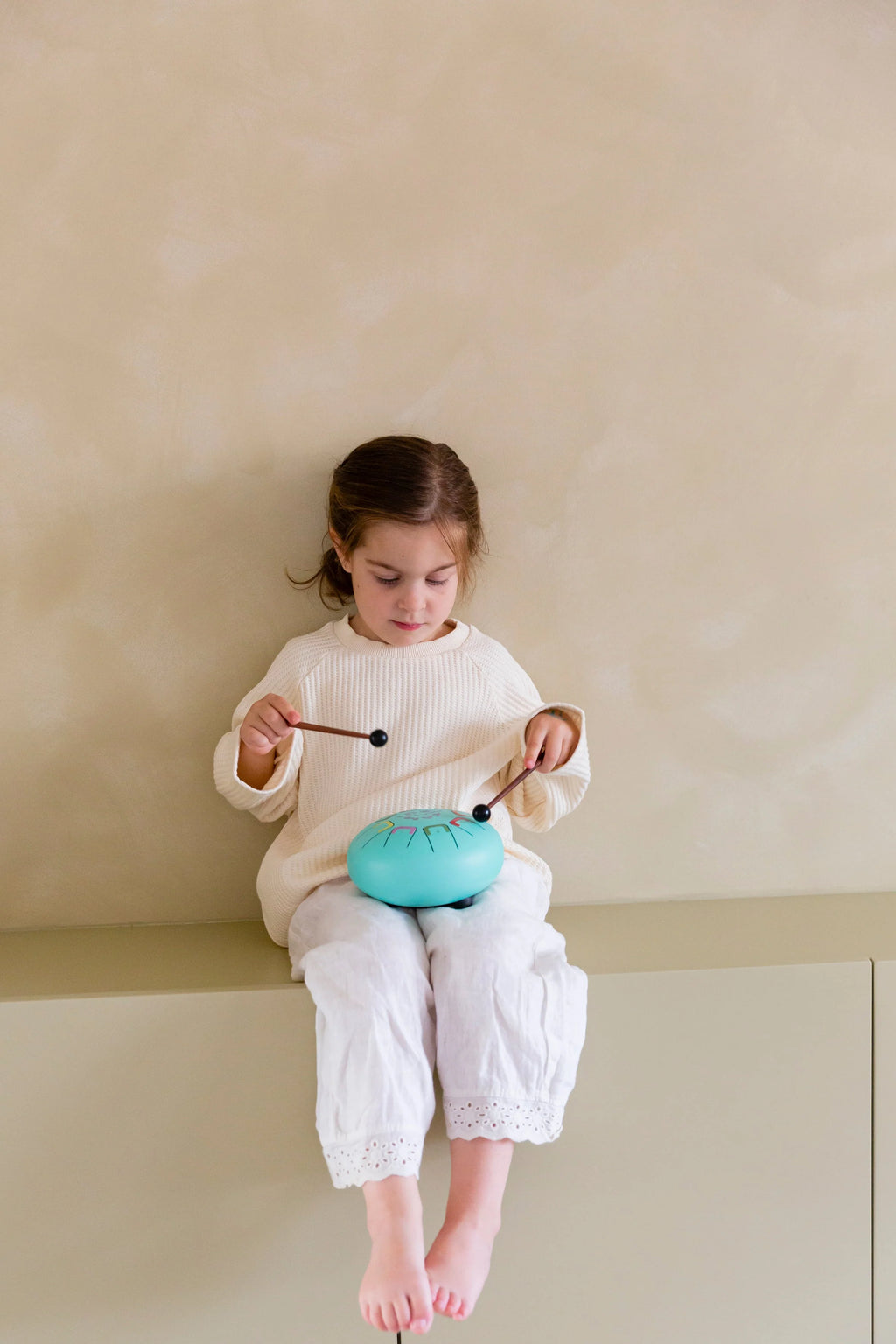 Child playing with a blue toy drum on a beige shelf
