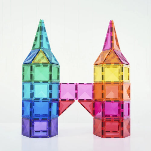 Two translucent acrylic magnetic building towers connected by a bridge, made from colorful square and triangular tiles in green, blue, purple, pink, yellow, and orange, set against a plain white background.