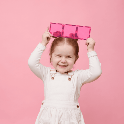 Child holding a pink Connetix tile on a pink background