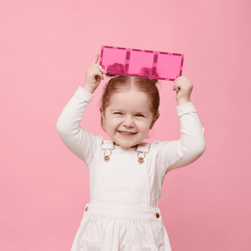 Child holding a pink Connetix tile on a pink background