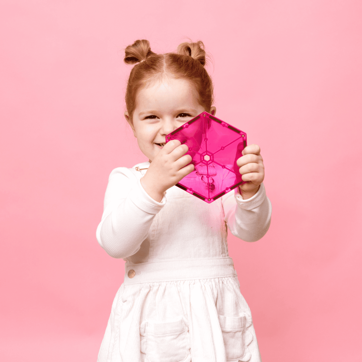 Child holding a pink transparent cube against a pink background