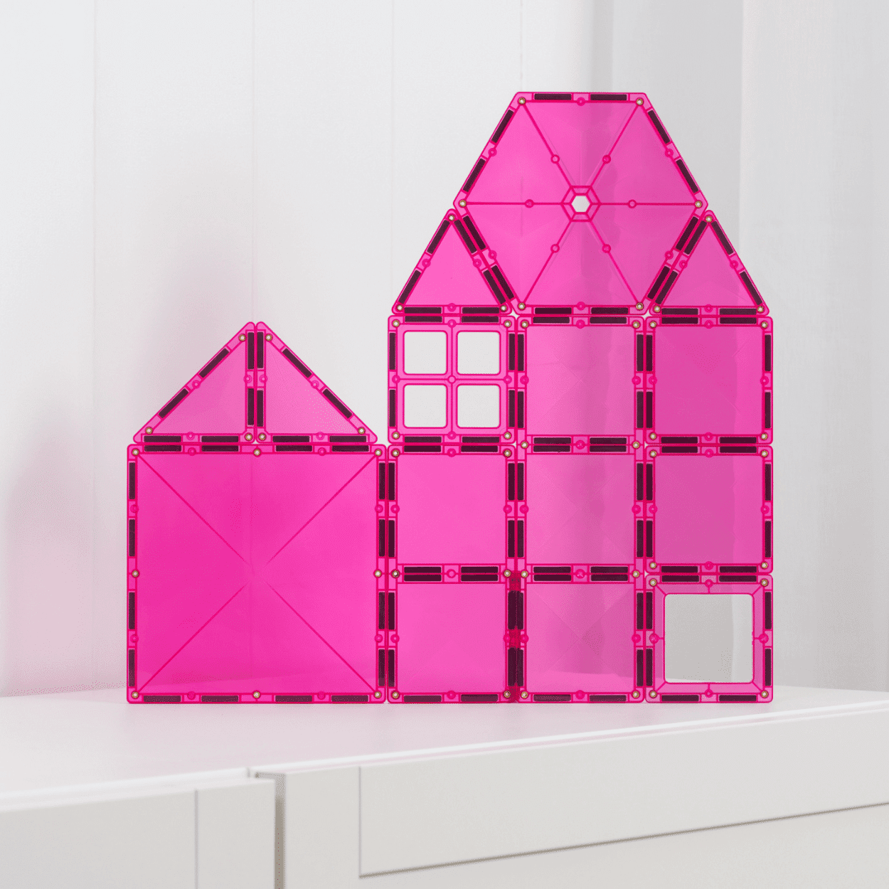 Pink transparent house-shaped building block set on a white surface with a light pink background