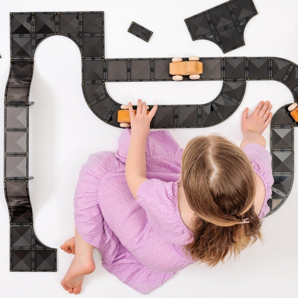 Child playing with a toy track set on a white surface