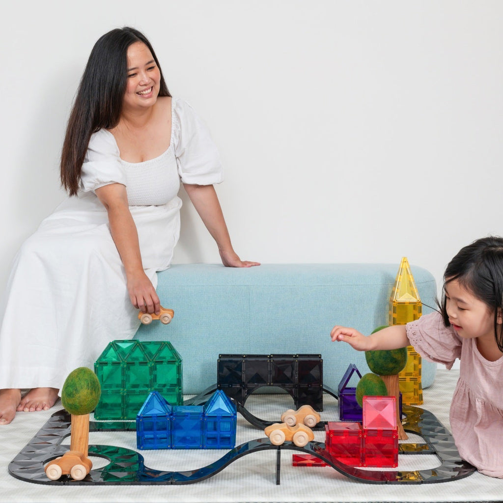 Woman and child playing with colorful building blocks on a white floor.
