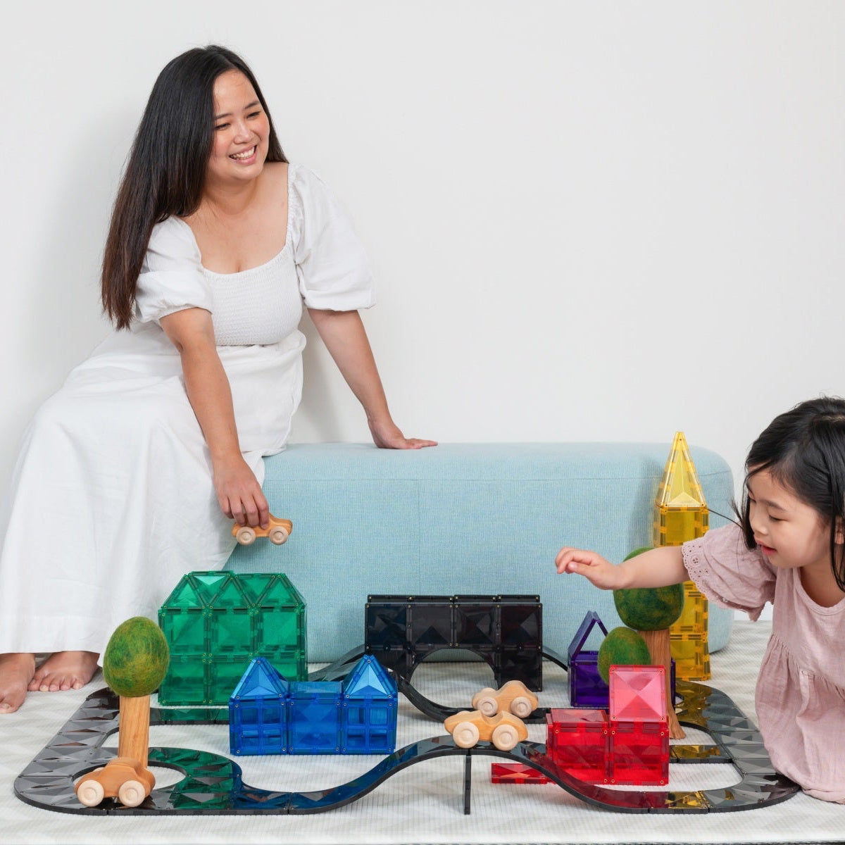Woman and child playing with colorful building blocks on a white floor.