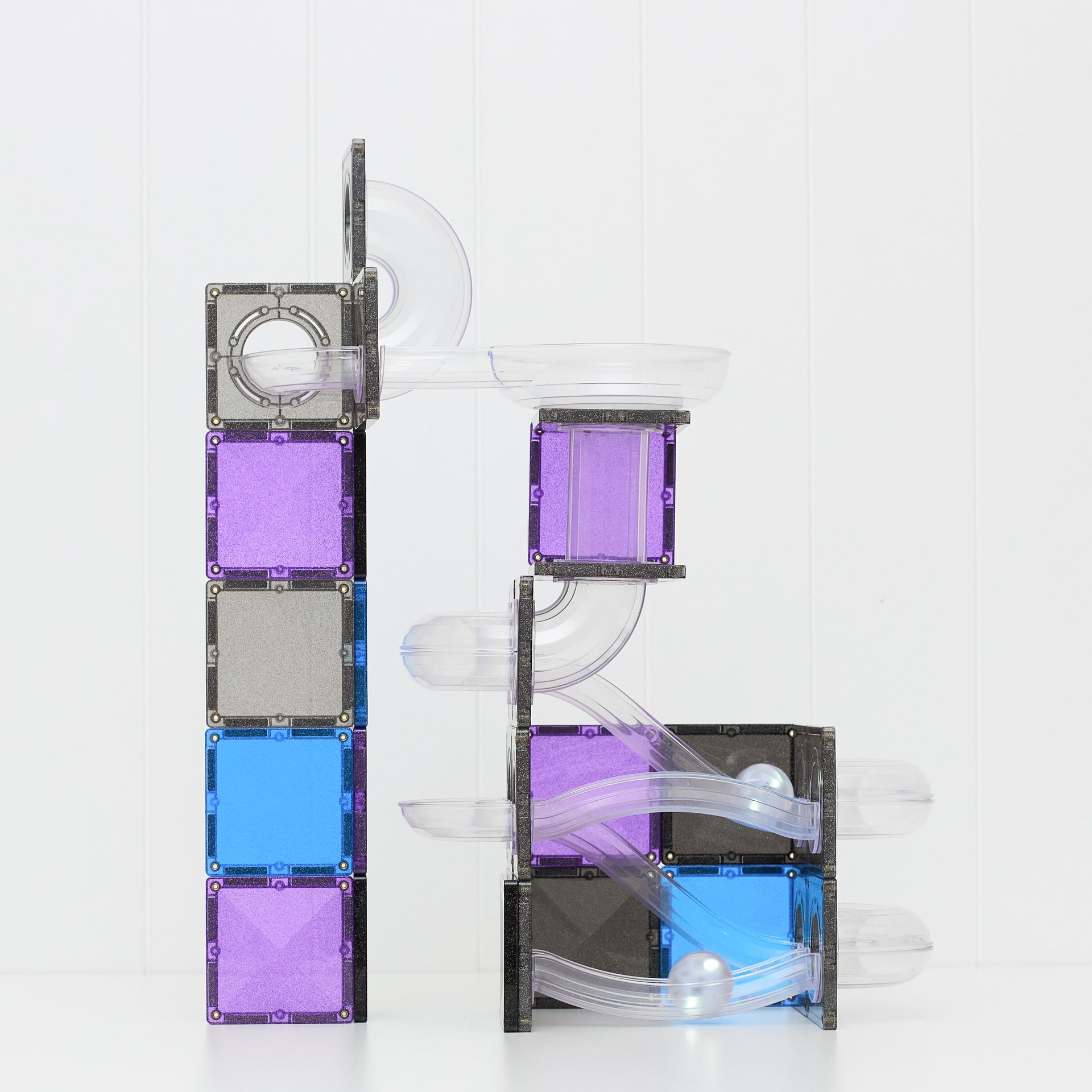 Magnetic building blocks set with clear plastic tubes and tracks, featuring purple, blue, and gray square tiles on a white background.
