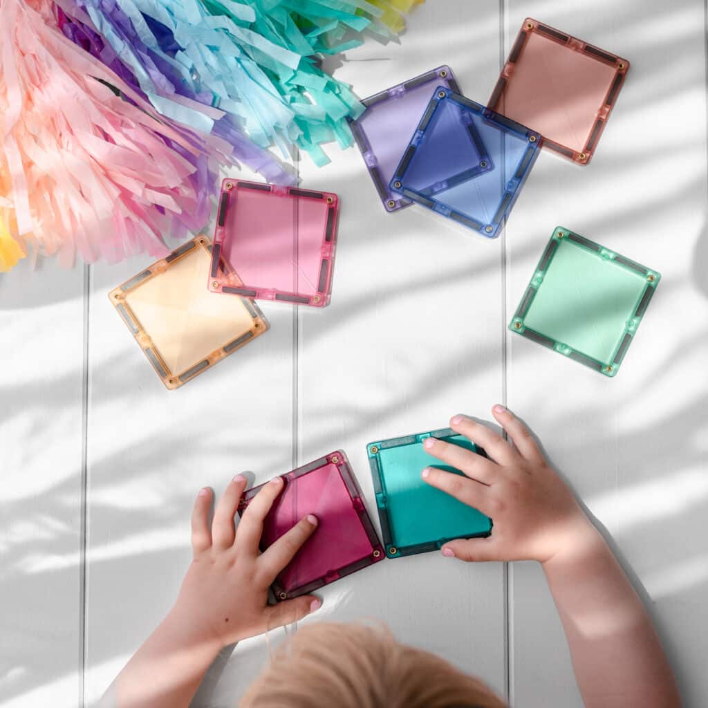 Colorful transparent square blocks on a light wooden surface with children's hands interacting with them.