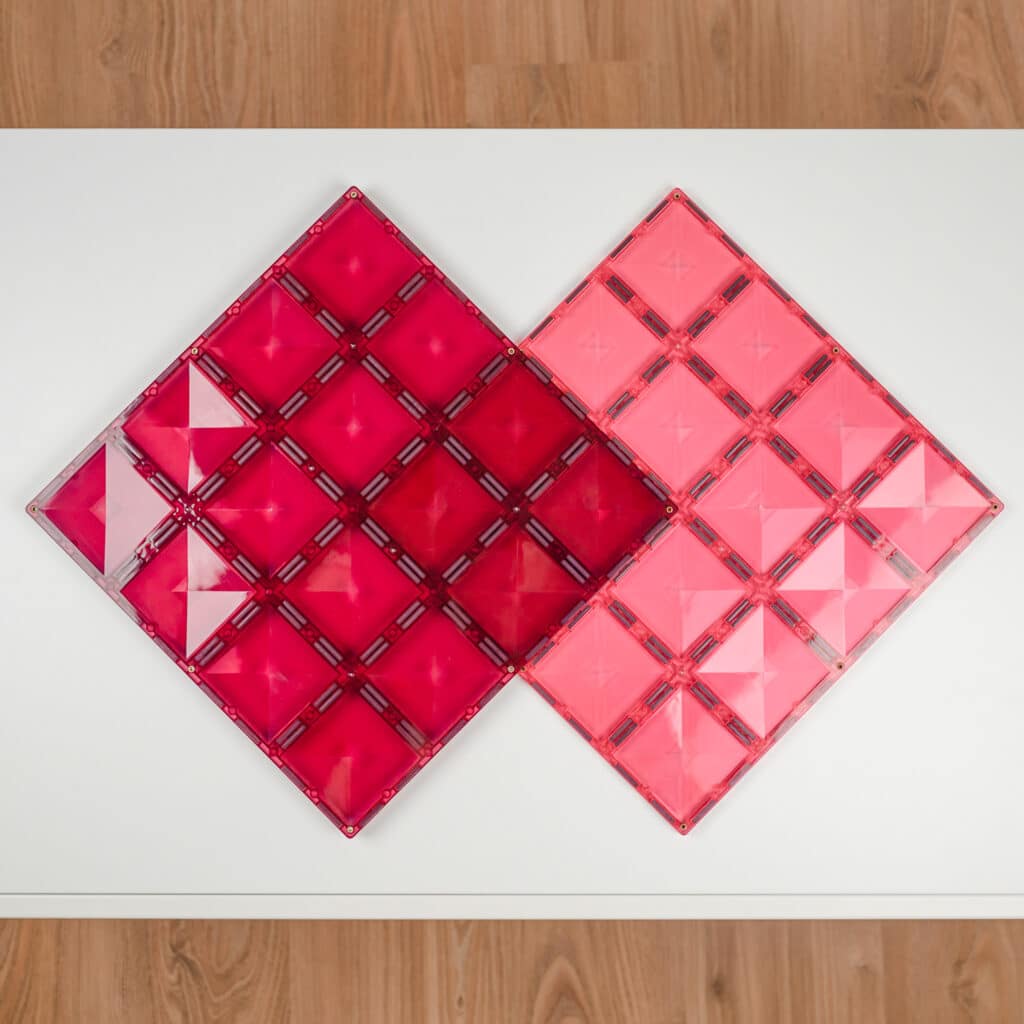 Two pink geometric tile designs on a white surface with wooden floor background